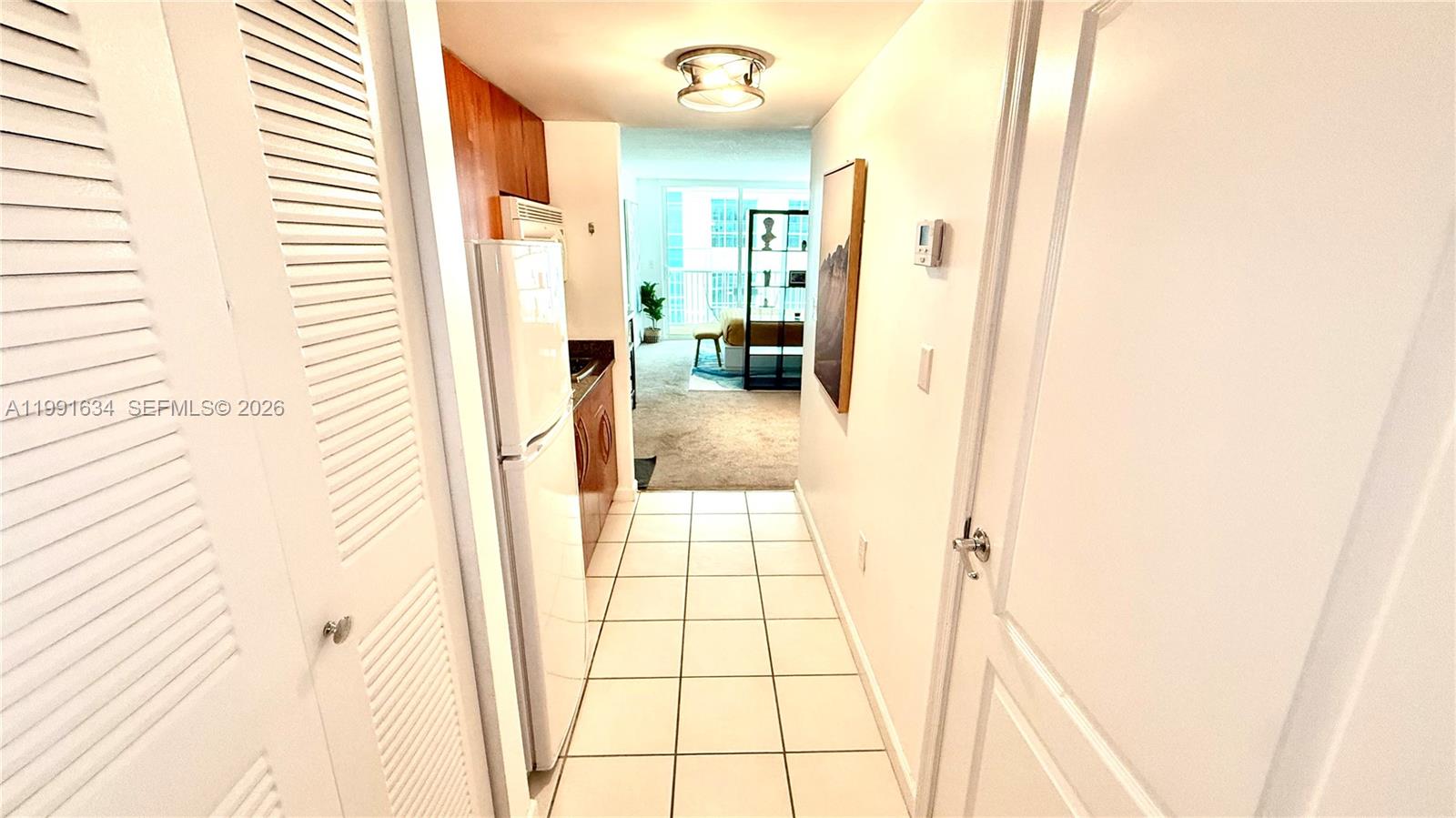 A narrow tiled hallway leads past a kitchen with a white refrigerator toward a bedroom — 1200 Brickell Bay Dr # 2216, Miami FL 33131, MIAMI, FL