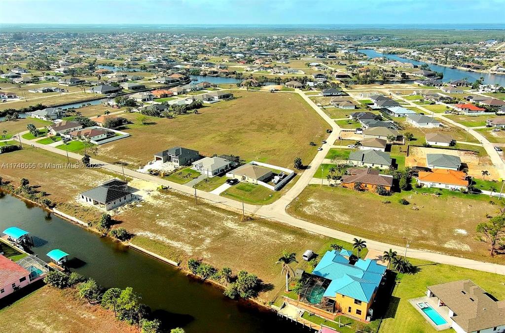 An aerial view shows a residential neighborhood with houses, canals, and vacant lots — 1939 NW 34TH PLACE, CAPE CORAL, FL