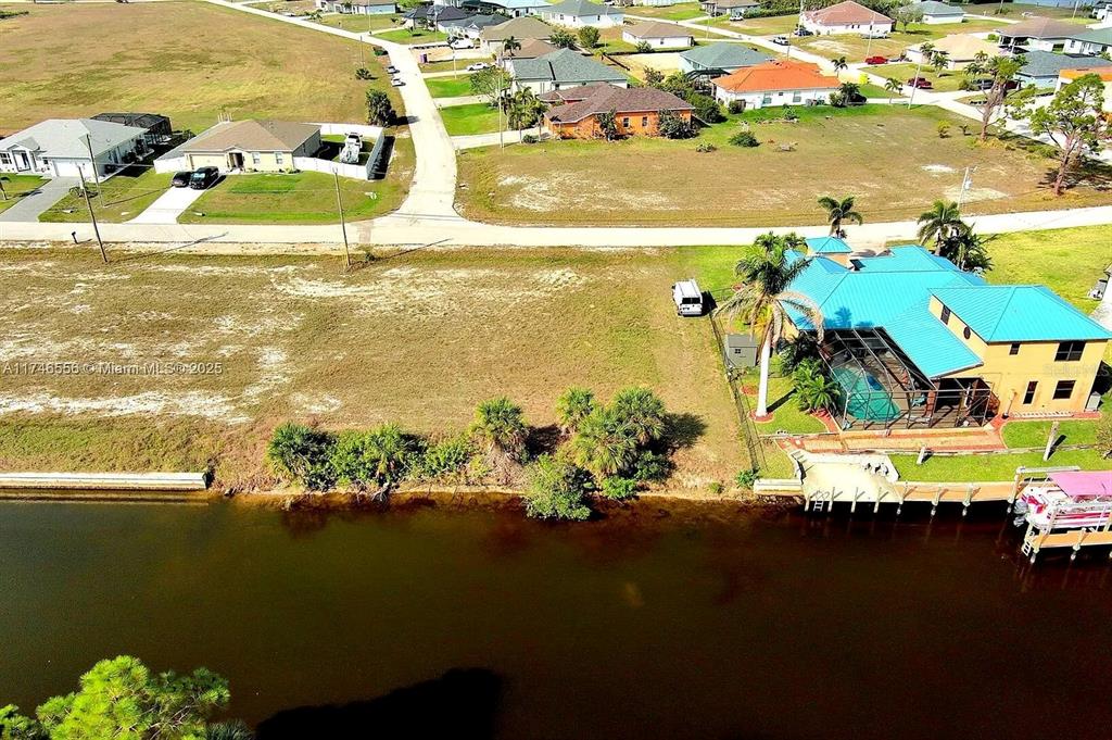An aerial view shows a waterfront lot next to a house with a blue roof — 1939 NW 34TH PLACE, CAPE CORAL, FL