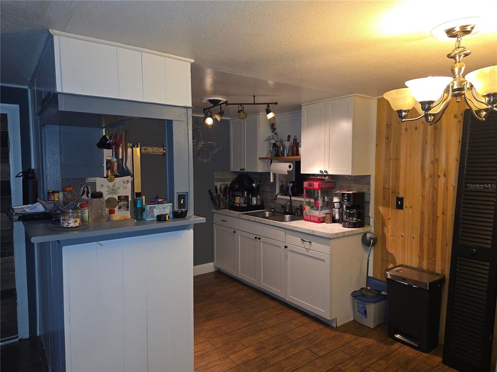 A kitchen features white cabinets, a breakfast bar, wood-look tile flooring, and a chandelier — 917 27TH STREET E, BRADENTON, FL