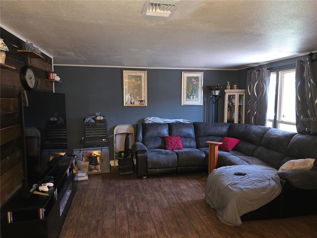 A living room features a dark sectional sofa, wood-look tile flooring, and a wood-paneled accent wall — 917 27TH STREET E, BRADENTON, FL