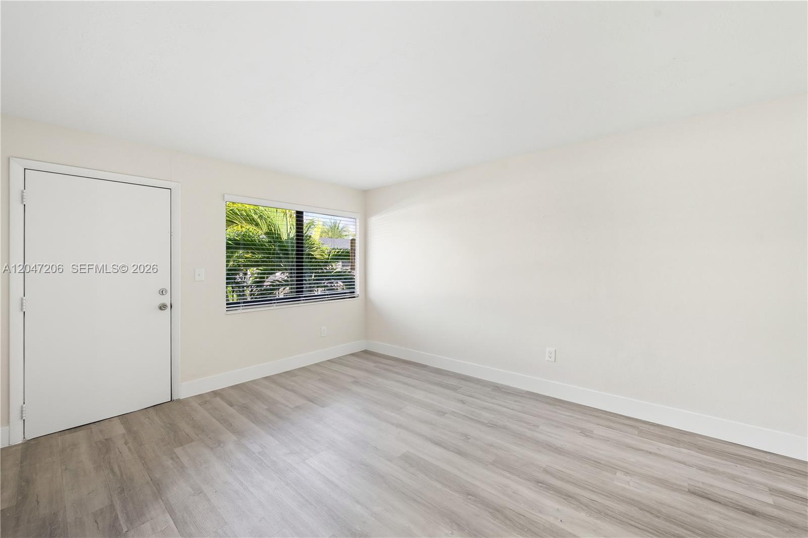 An empty room features light-colored walls, wood-look flooring, a single window, and a white door — 1330 W 29th St # 34, Hialeah FL 33012, HIALEAH, FL
