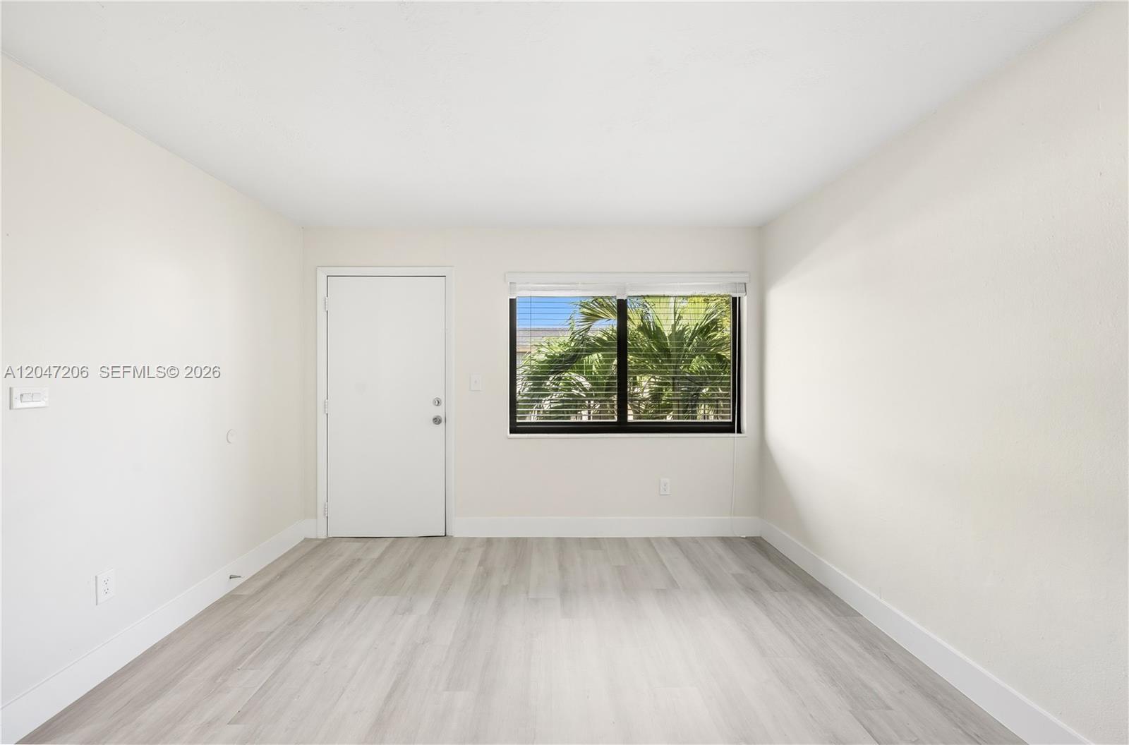 An empty room features light wood-look flooring, white walls, a single door, and a window — 1330 W 29th St # 34, Hialeah FL 33012, HIALEAH, FL