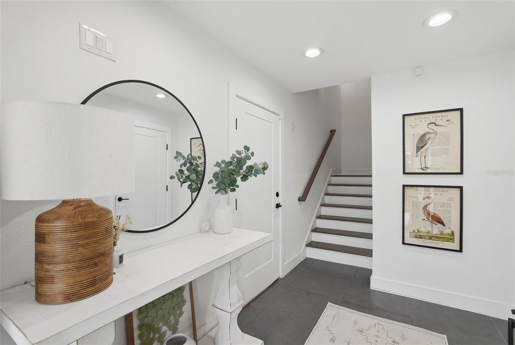 A bright entryway features a white console table, a round mirror, and stairs with dark treads — 1727 MARYLAND AVENUE NE, ST PETERSBURG, FL