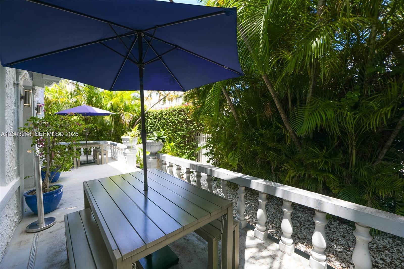 A patio features two dining tables with umbrellas, a stone balustrade, and lush tropical landscaping — 1618 Michigan Ave # 38, Miami Beach FL 33139, MIAMI BEACH, FL