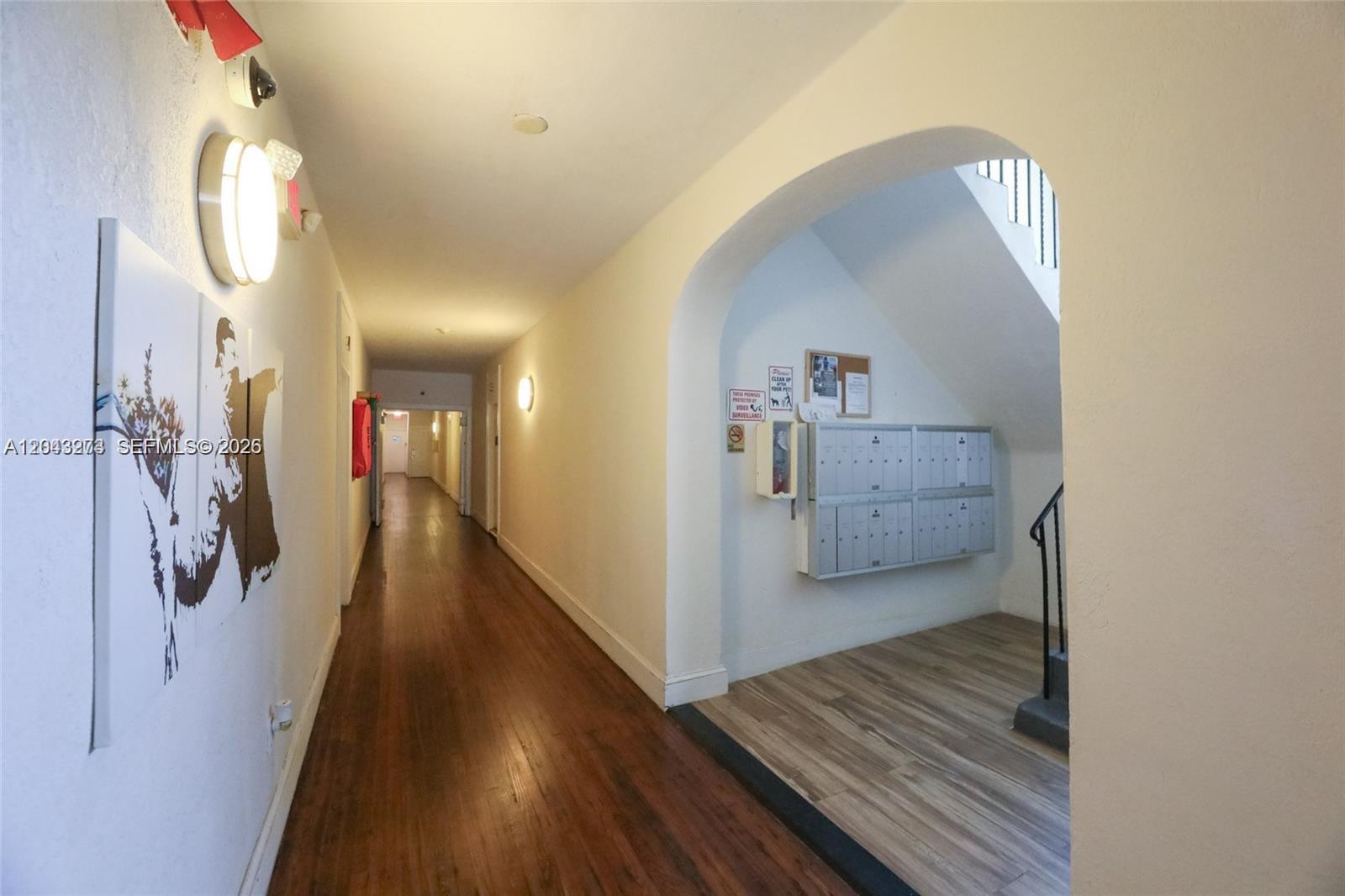 A hallway with wood flooring leads to a stairwell area featuring mailboxes and wall art — 1618 Michigan Ave # 38, Miami Beach FL 33139, MIAMI BEACH, FL