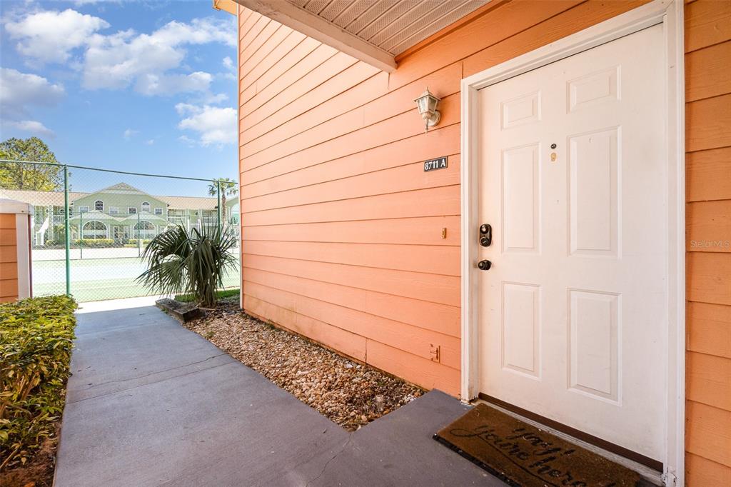 An exterior view of a peach-colored building entrance with a white door and walkway — 8711 ROCKINGHAM TERRACE UNIT A, KISSIMMEE, FL
