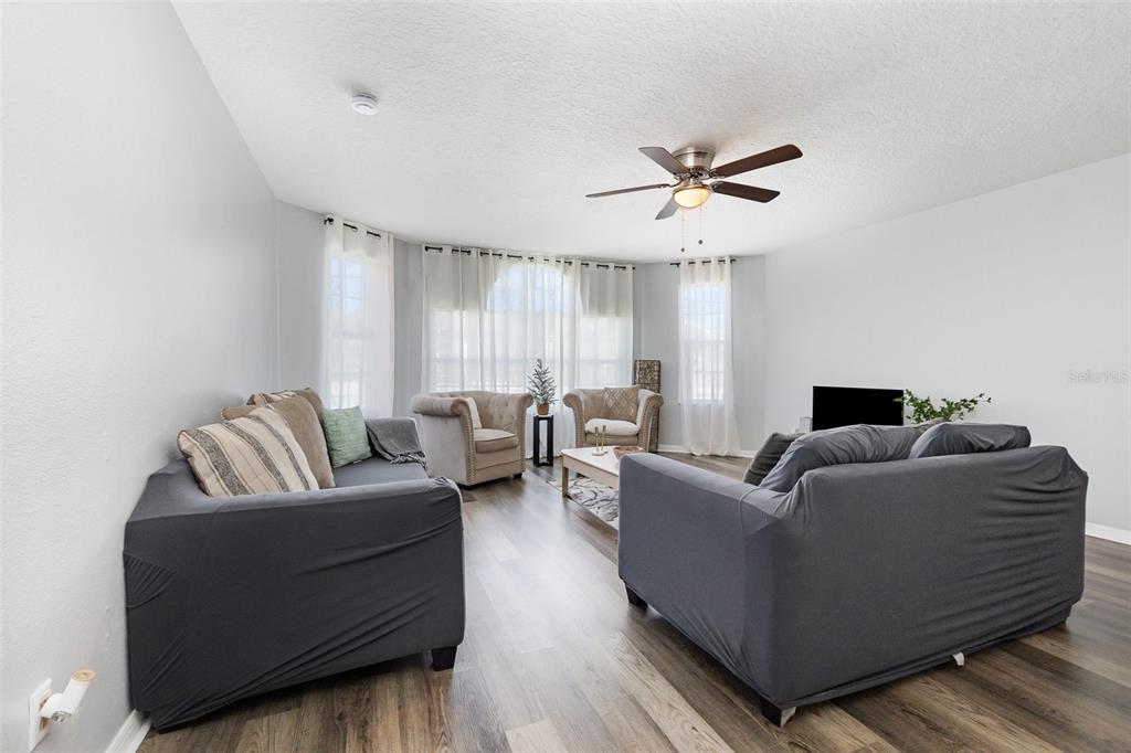 A living room features two grey sofas, two armchairs, a coffee table, and wood flooring — 8711 ROCKINGHAM TERRACE UNIT A, KISSIMMEE, FL
