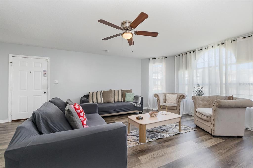 A living room features gray sofas, beige armchairs, a coffee table, and wood-look flooring — 8711 ROCKINGHAM TERRACE UNIT A, KISSIMMEE, FL