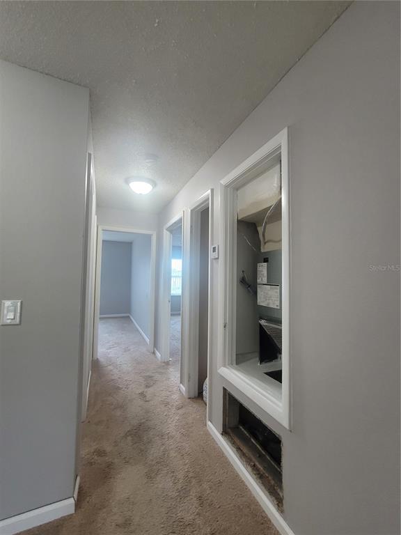 A hallway with carpeted floors leads to two doorways, featuring an open HVAC utility closet — 9900 SWEEPSTAKES LANE UNIT 3, ORLANDO, FL