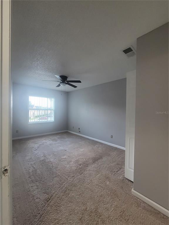 An empty bedroom with gray walls, beige carpeting, a ceiling fan, and a window — 9900 SWEEPSTAKES LANE UNIT 3, ORLANDO, FL