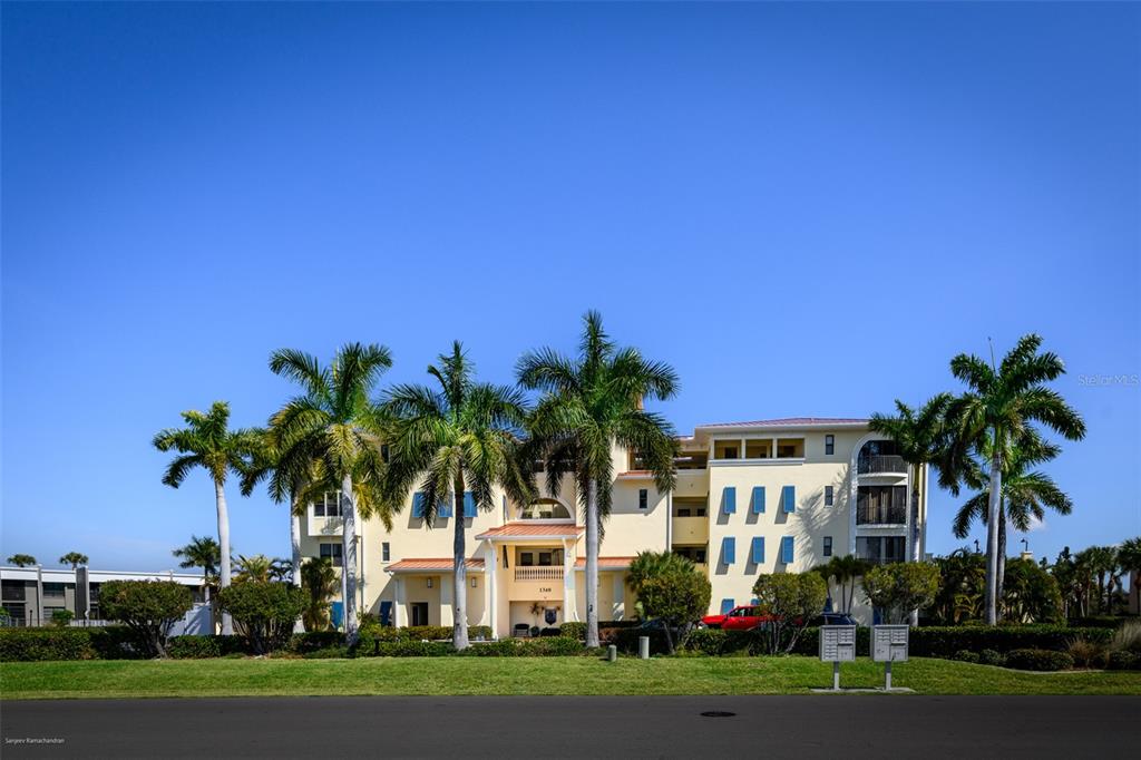 A multi-story beige apartment building stands behind a grassy lawn with several tall palm trees — 1340 ROCK DOVE COURT UNIT 144, PUNTA GORDA, FL