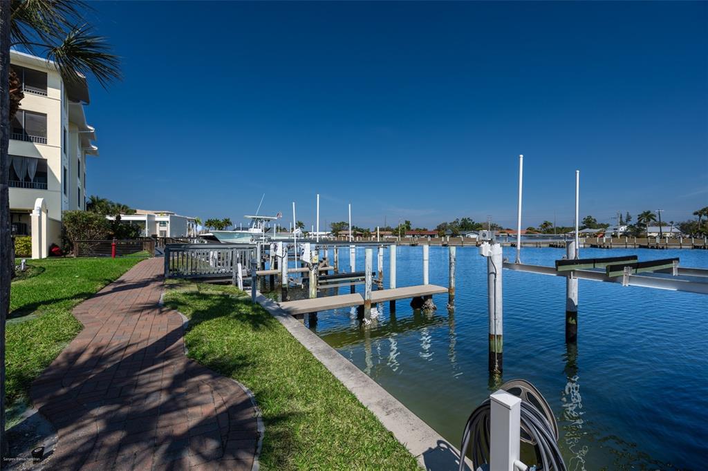 A brick walkway leads along a grassy bank toward boat docks on a sunny canal — 1340 ROCK DOVE COURT UNIT 144, PUNTA GORDA, FL