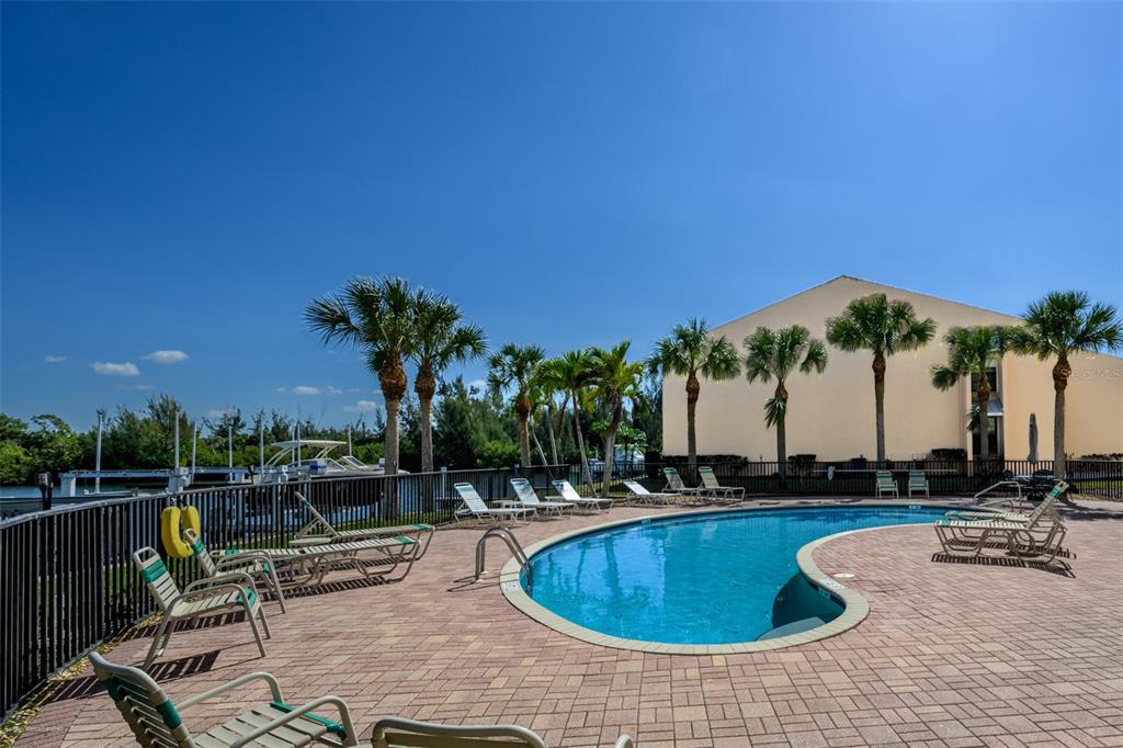 A swimming pool with lounge chairs sits on a paved deck beside a building — 1340 ROCK DOVE COURT UNIT 144, PUNTA GORDA, FL