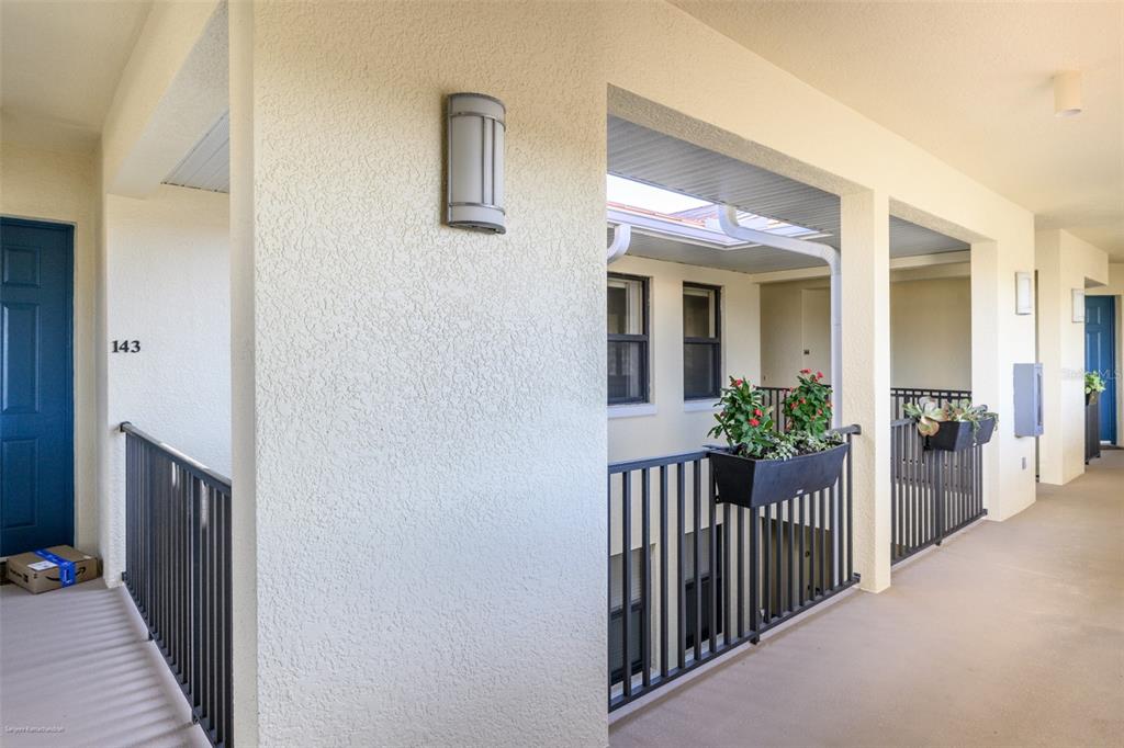An outdoor apartment building hallway with a blue door, black railings, and potted plants — 1340 ROCK DOVE COURT UNIT 144, PUNTA GORDA, FL