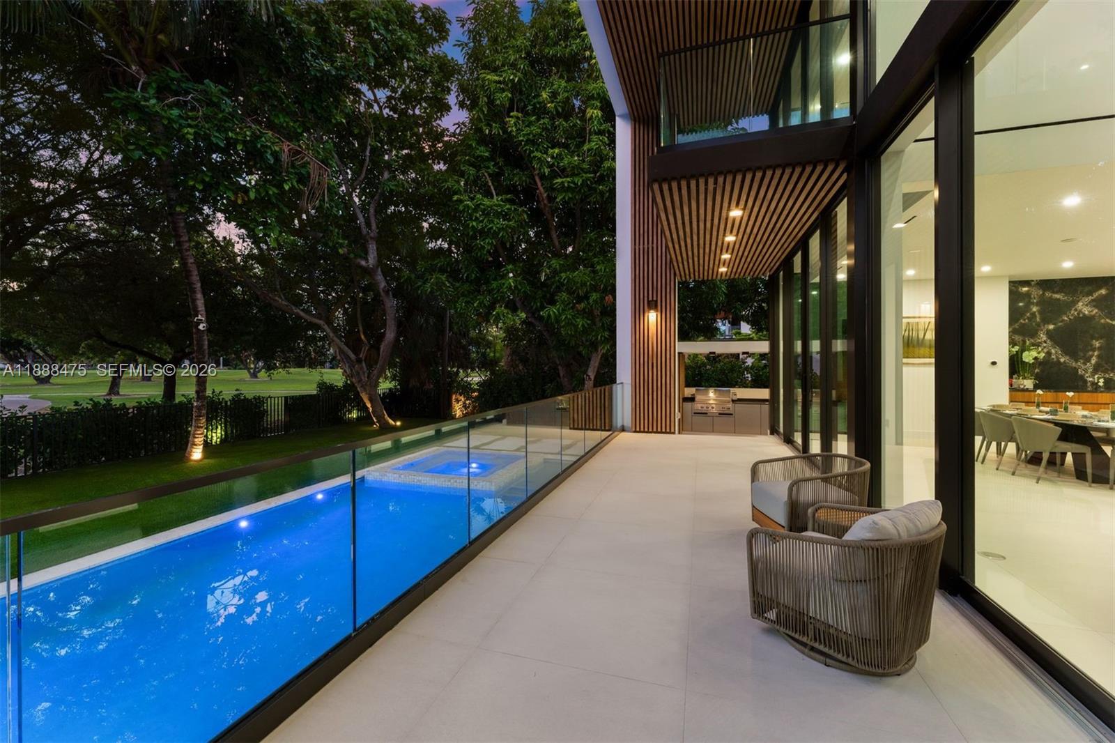 A modern patio features a glass-railed pool, outdoor seating, and a view of trees — 3114 Prairie Ave, Miami Beach FL 33140, MIAMI BEACH, FL