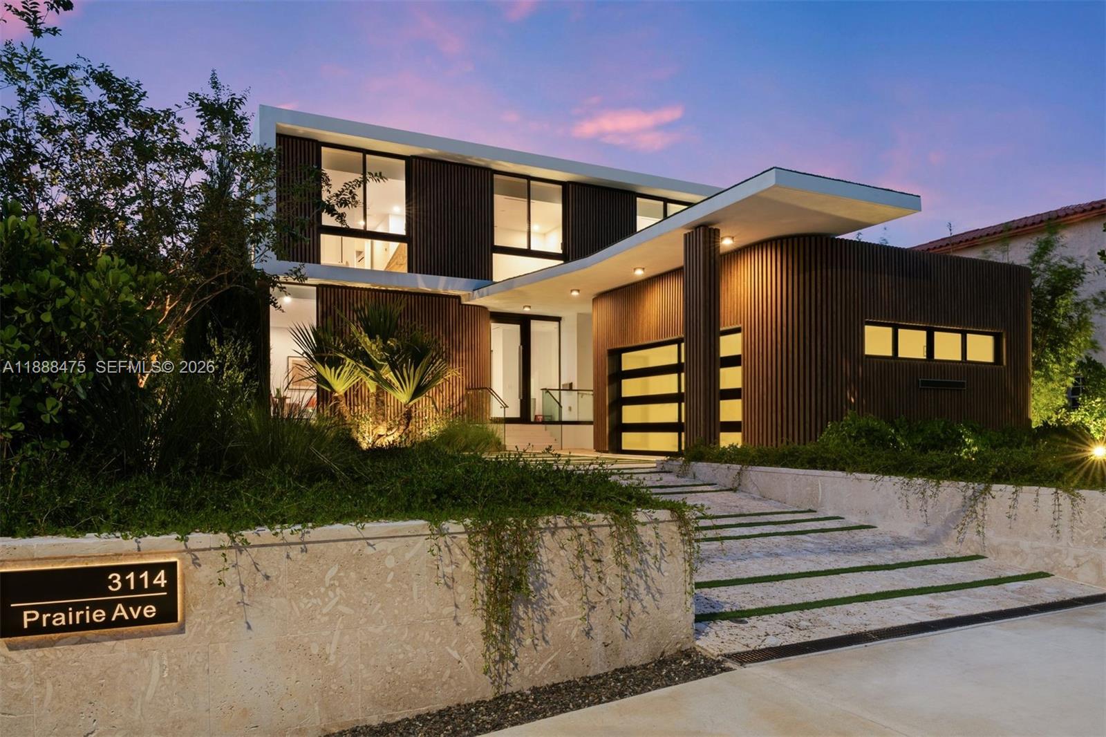 A modern two-story house with vertical wood siding and a stone retaining wall at dusk — 3114 Prairie Ave, Miami Beach FL 33140, MIAMI BEACH, FL