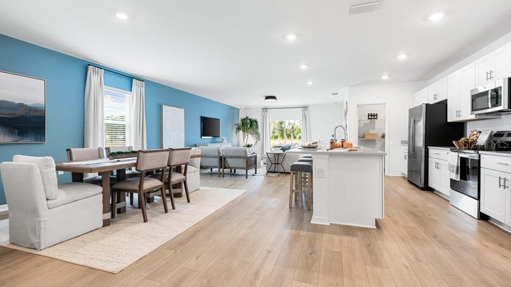 An open-concept living area features a dining space, kitchen with white cabinets, and blue wall — 220 STREAMWATER WAY, GROVELAND, FL