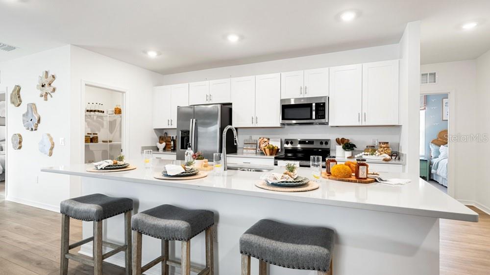 A modern kitchen features white cabinetry, stainless steel appliances, and a large quartz-topped island — 220 STREAMWATER WAY, GROVELAND, FL