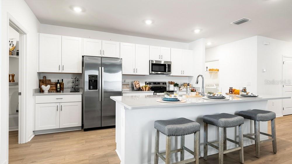 A modern kitchen features white cabinetry, stainless steel appliances, and a large island with stools — 220 STREAMWATER WAY, GROVELAND, FL