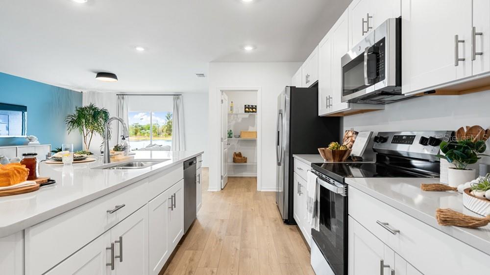 A modern kitchen features white cabinetry, stainless steel appliances, a large island, and light flooring — 220 STREAMWATER WAY, GROVELAND, FL