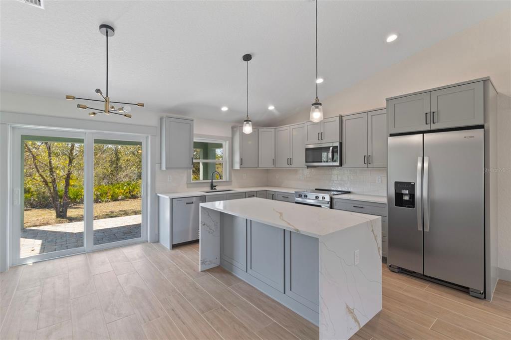 A modern kitchen features gray cabinets, a white marble-topped island, and a sliding glass door — 4117 JOSEPH STREET, PORT CHARLOTTE, FL