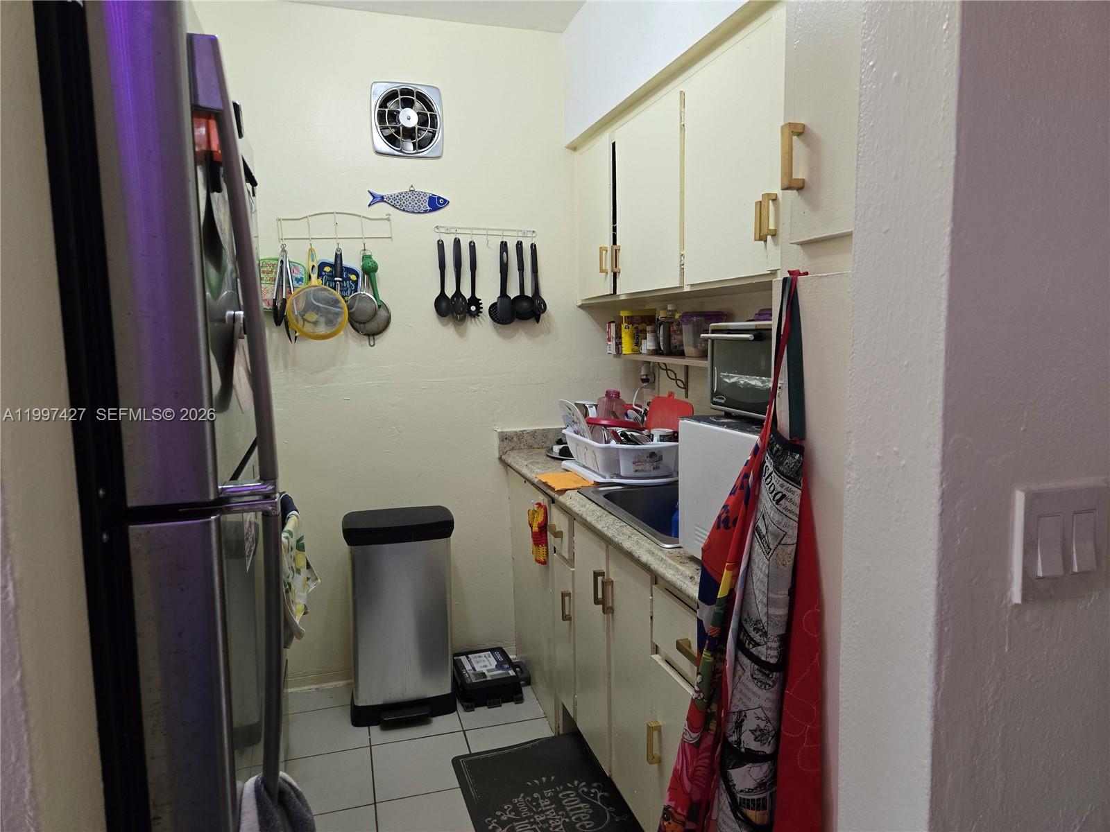 A small galley kitchen features light-colored cabinets, a stainless steel refrigerator, and a trash can — 820 SW 11th Ave # 5B, Hallandale Beach FL 33009, HALLANDALE BEACH, FL