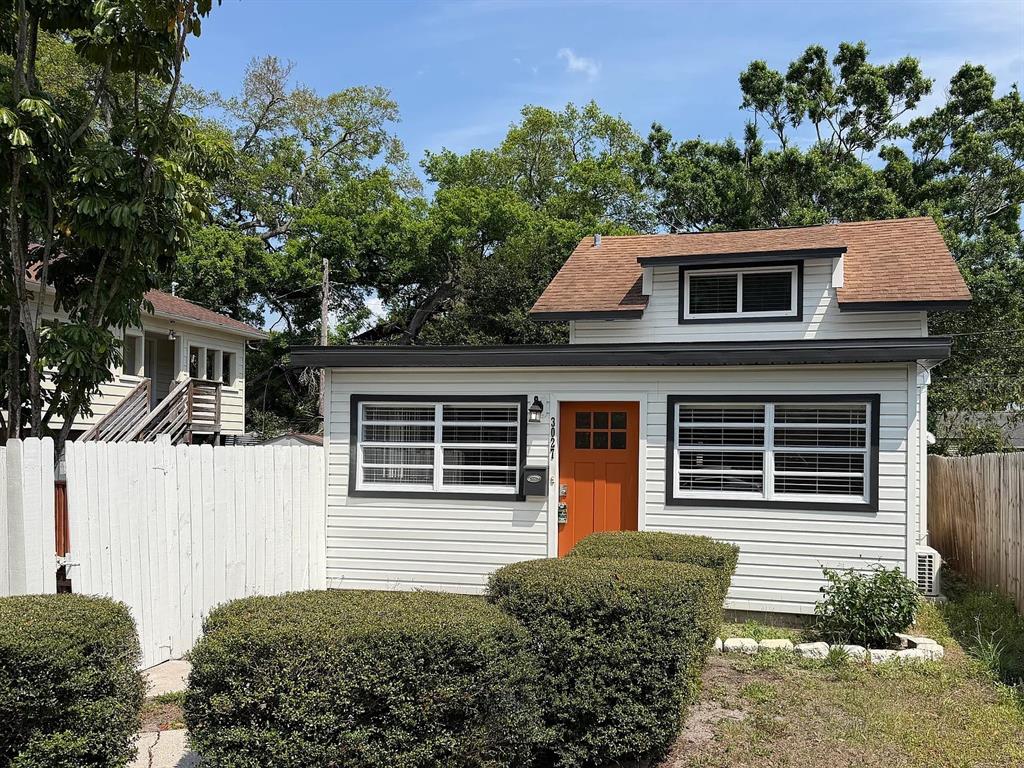 A small, white-sided house with a brown roof, orange door, and manicured hedges in front — 3027 MELTON STREET N, ST PETERSBURG, FL