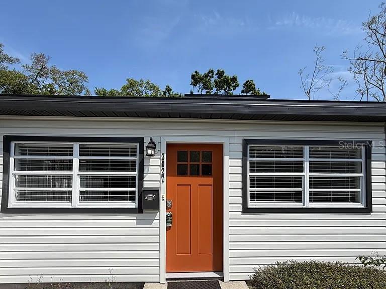 A white house exterior features a bright orange front door and two large windows — 3027 MELTON STREET N, ST PETERSBURG, FL