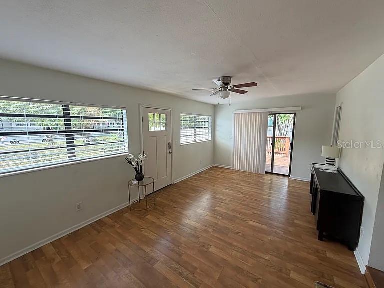 A living room features light wood-look flooring, a ceiling fan, and a sliding glass door — 3027 MELTON STREET N, ST PETERSBURG, FL