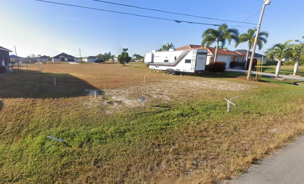A vacant grassy lot features several white survey stakes and a large parked travel trailer — 2458 NW 22ND STREET, CAPE CORAL, FL