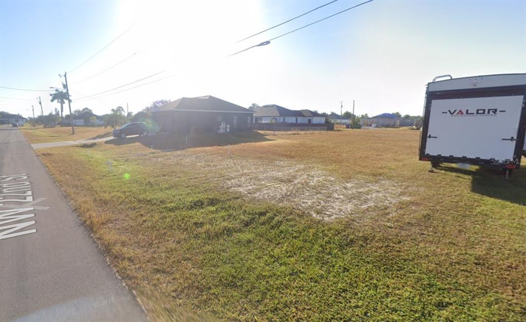 A vacant, grassy residential lot sits next to a road and a parked trailer — 2458 NW 22ND STREET, CAPE CORAL, FL