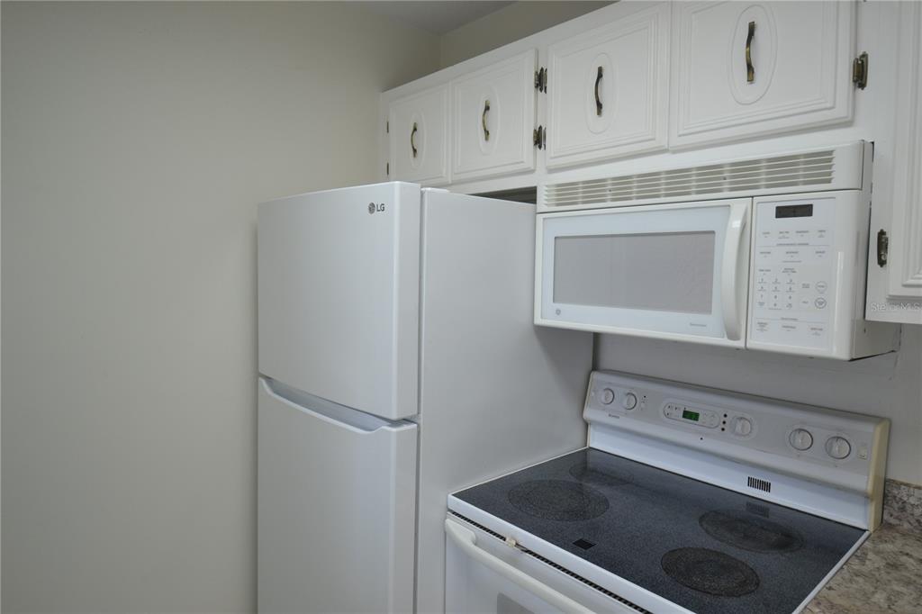 A white kitchen features a refrigerator, over-the-range microwave, and an electric stove — 329 MOORINGS COVE DRIVE, TARPON SPRINGS, FL