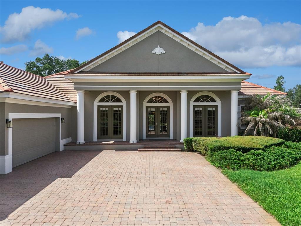 A single-story house with a brick driveway, three arched glass doors, and four white columns — 6533 CARTMEL LN, WINDERMERE, FL