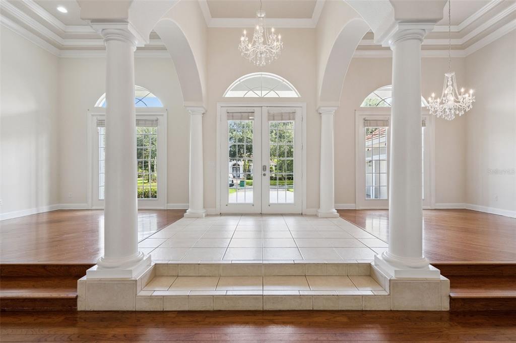 A bright entryway features a tiled raised platform, white columns, arched windows, and crystal chandeliers — 6533 CARTMEL LN, WINDERMERE, FL