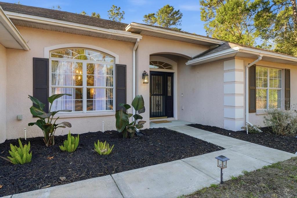 The exterior of a single-story house features a front entrance, arched windows, and landscaping — 21 LOBELIA COURT, HOMOSASSA, FL