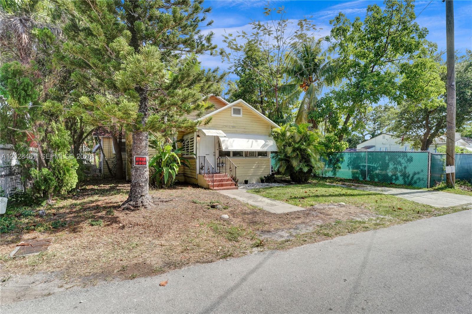 A small, yellow, single-story house with a front porch sits behind a chain-link fence — 259 NE 57th St, Miami FL 33137, MIAMI, FL