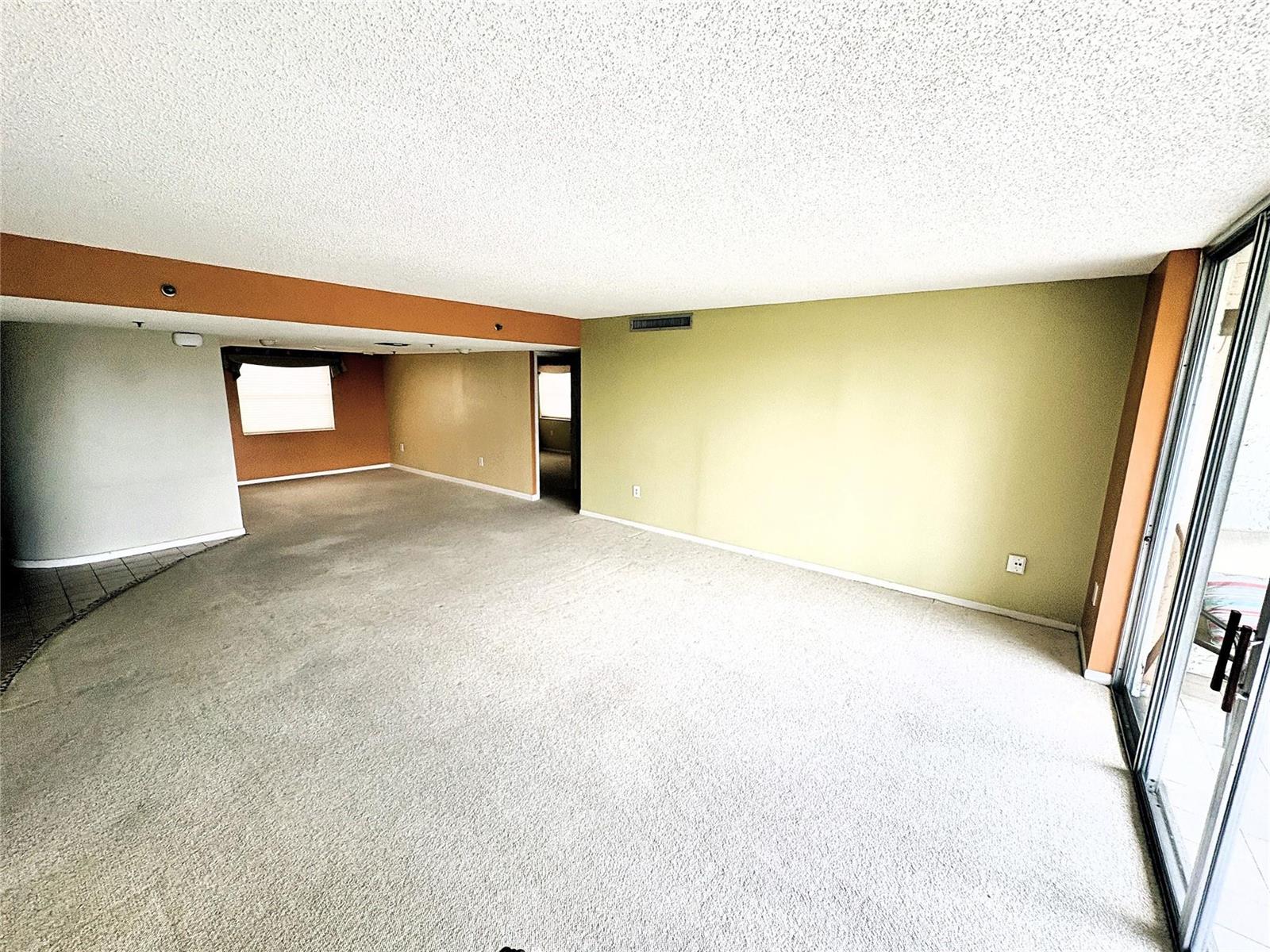 An empty living room features beige carpet, a popcorn ceiling, and walls painted in multiple colors — 3940 Inverrary Boulevard # 701a, Lauderhill FL 33319, LAUDERHILL, FL