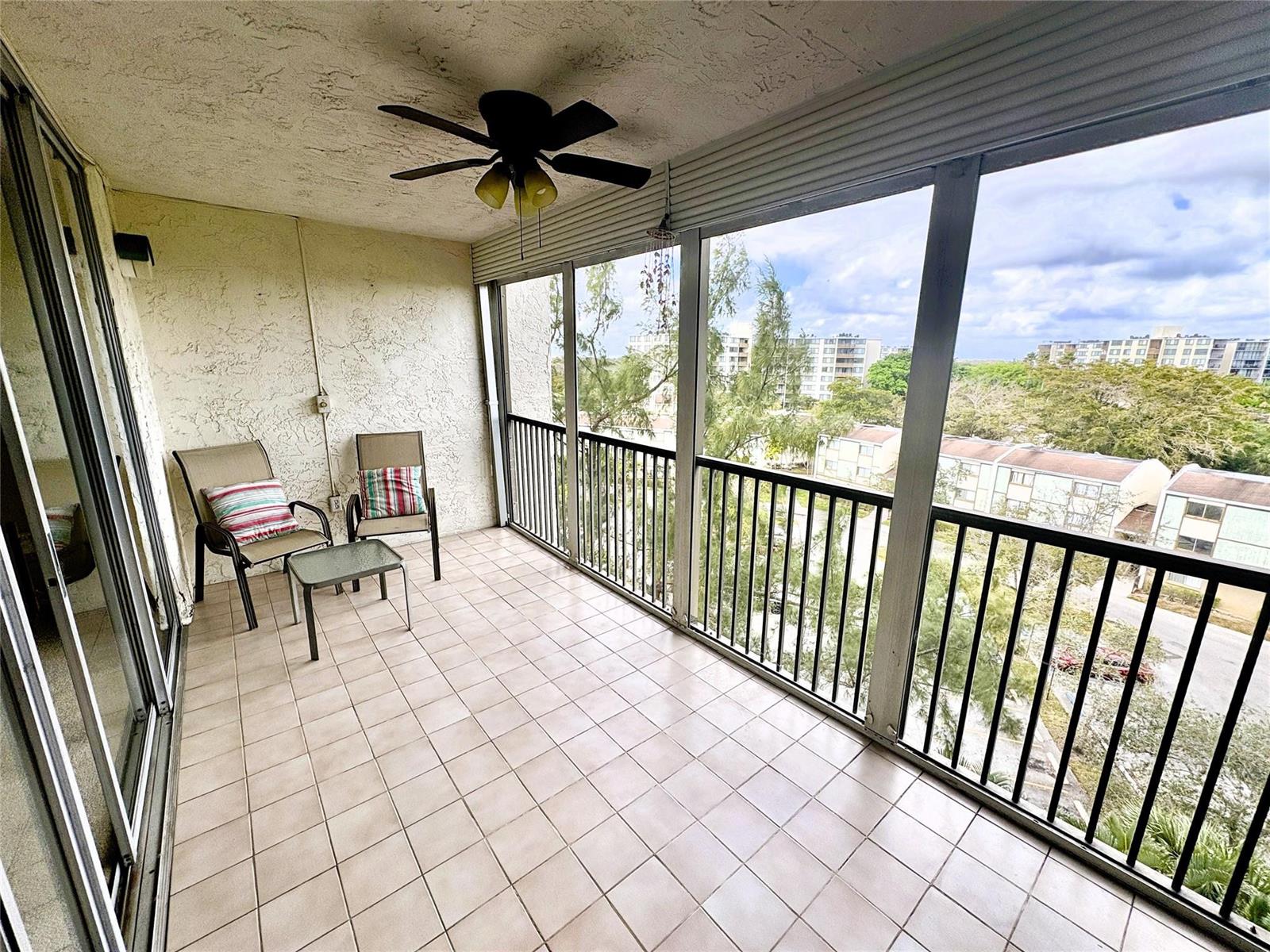 A covered balcony features tiled flooring, two chairs with a small table, and metal railings — 3940 Inverrary Boulevard # 701a, Lauderhill FL 33319, LAUDERHILL, FL