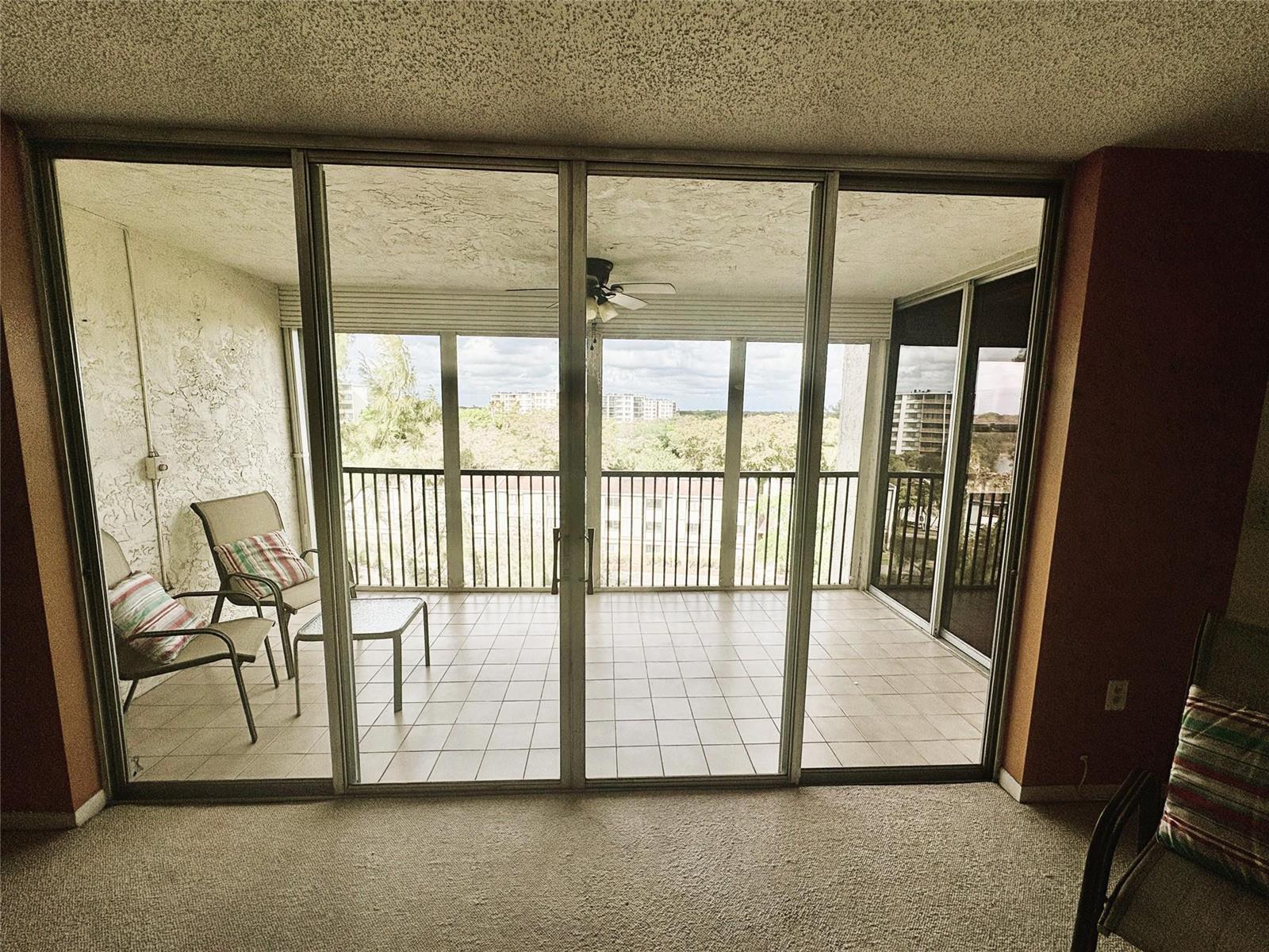 A carpeted room looks through large sliding glass doors onto a tiled balcony with outdoor furniture — 3940 Inverrary Boulevard # 701a, Lauderhill FL 33319, LAUDERHILL, FL