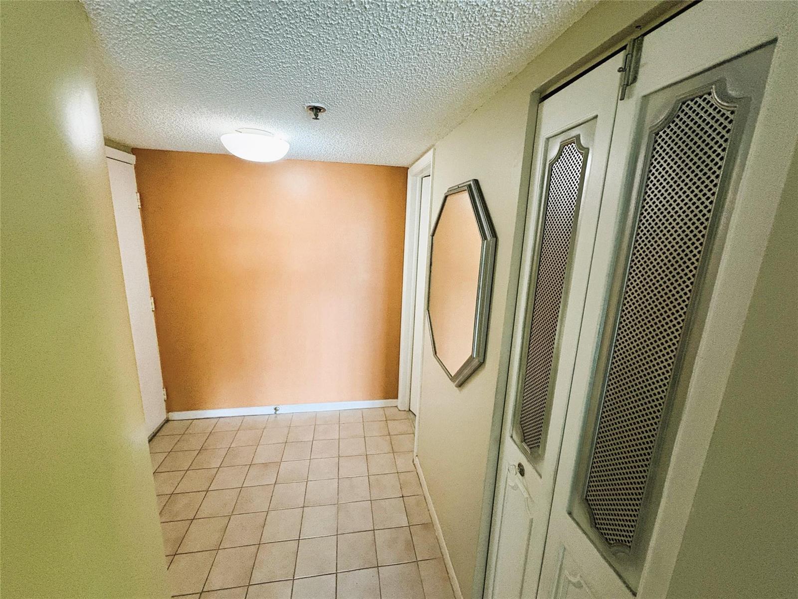 A hallway with beige tile flooring, an orange accent wall, and a white louvered closet — 3940 Inverrary Boulevard # 701a, Lauderhill FL 33319, LAUDERHILL, FL