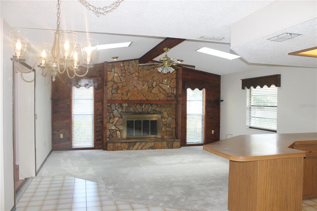 A living room features a stone fireplace, wood-paneled walls, a ceiling fan, and carpeted flooring — 8513 WINTER HAVEN DRIVE, HUDSON, FL