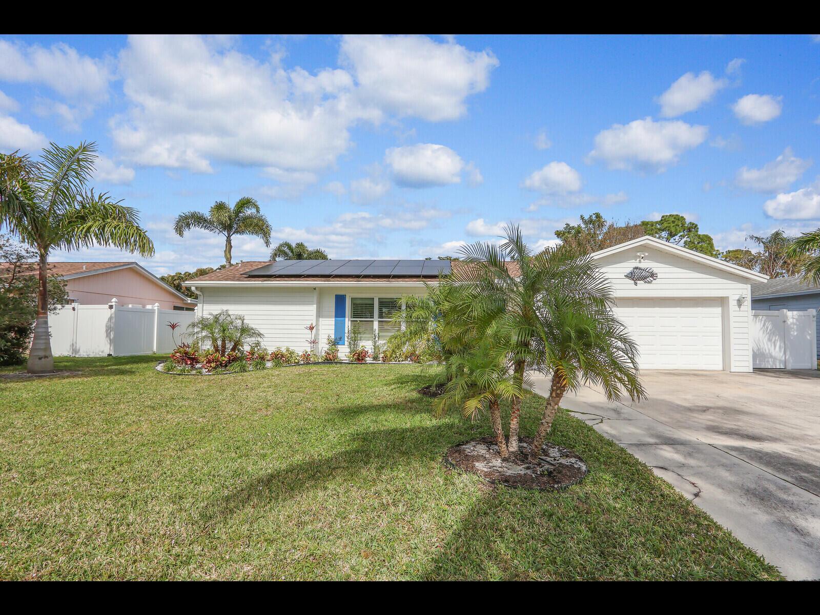 A single-story white house with solar panels, a garage, and palm trees in the yard — 609 Oak Terrace, Jupiter FL 33458, JUPITER, FL
