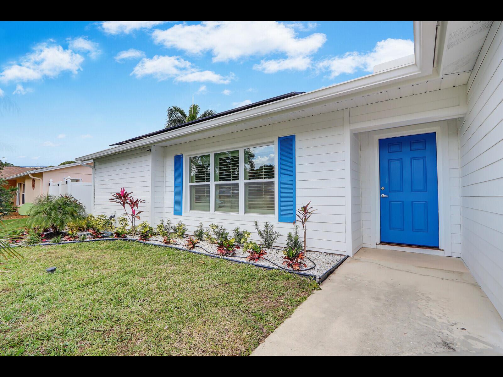 A white house exterior features a bright blue front door and matching window shutters — 609 Oak Terrace, Jupiter FL 33458, JUPITER, FL