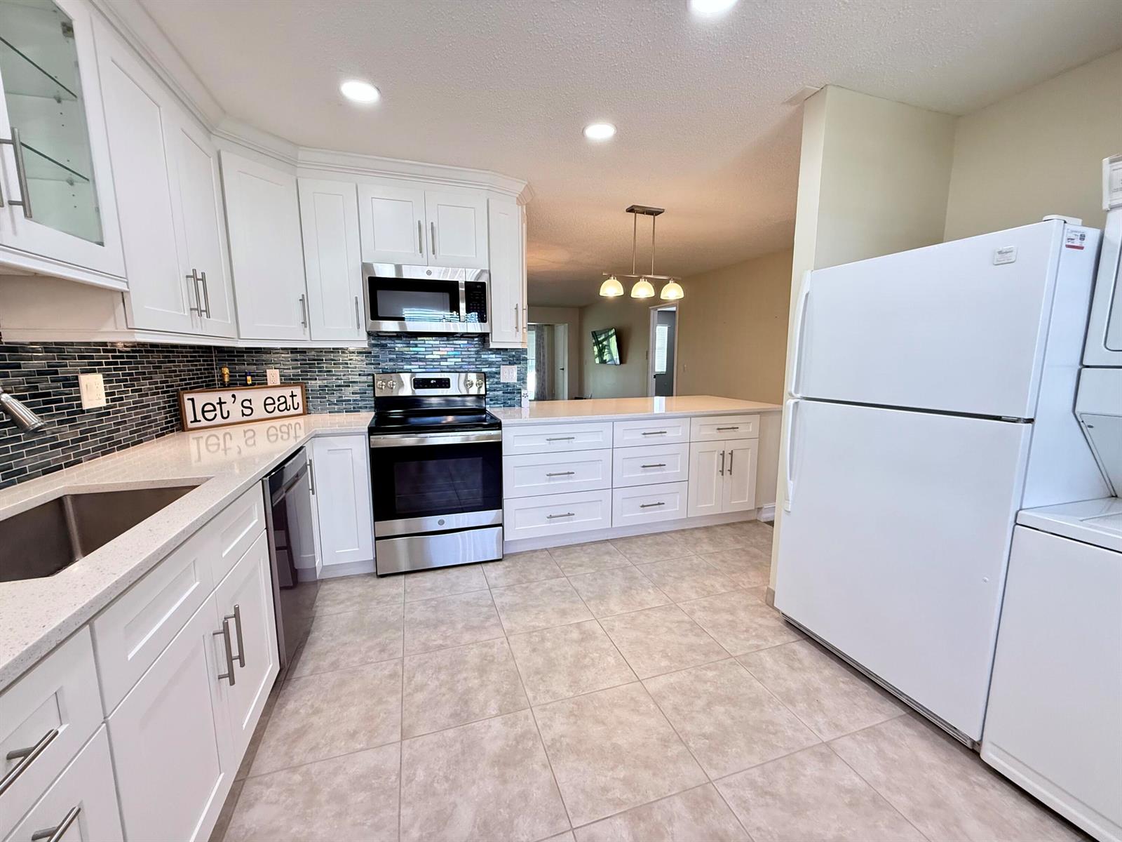 A kitchen features white cabinets, stainless steel appliances, a tiled backsplash, and light-colored countertops — 1740 NW 19th Terrace # 202, Delray Beach FL 33445, DELRAY BEACH, FL