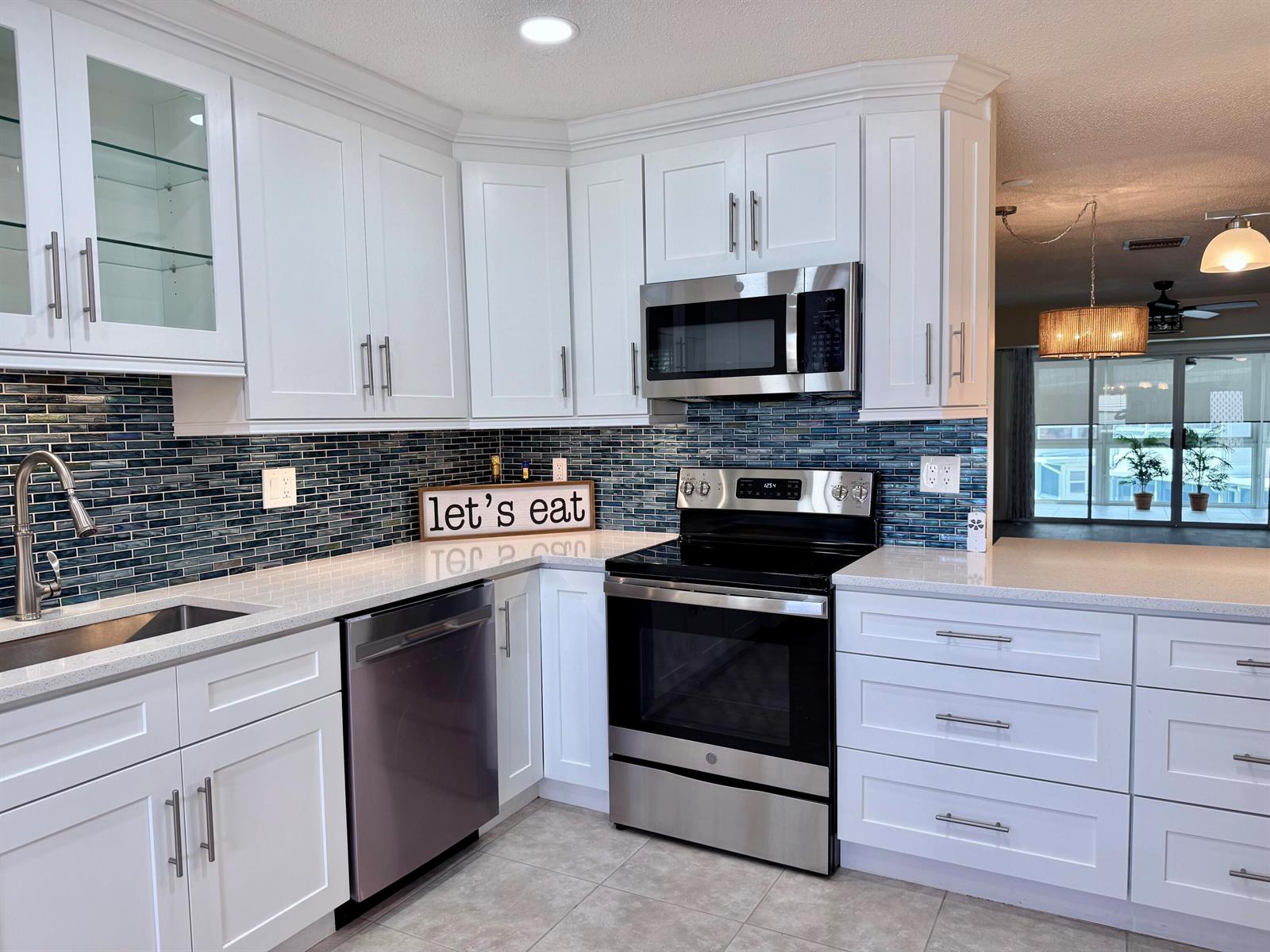 A kitchen featuring white cabinets, stainless steel appliances, quartz countertops, and a blue glass backsplash — 1740 NW 19th Terrace # 202, Delray Beach FL 33445, DELRAY BEACH, FL