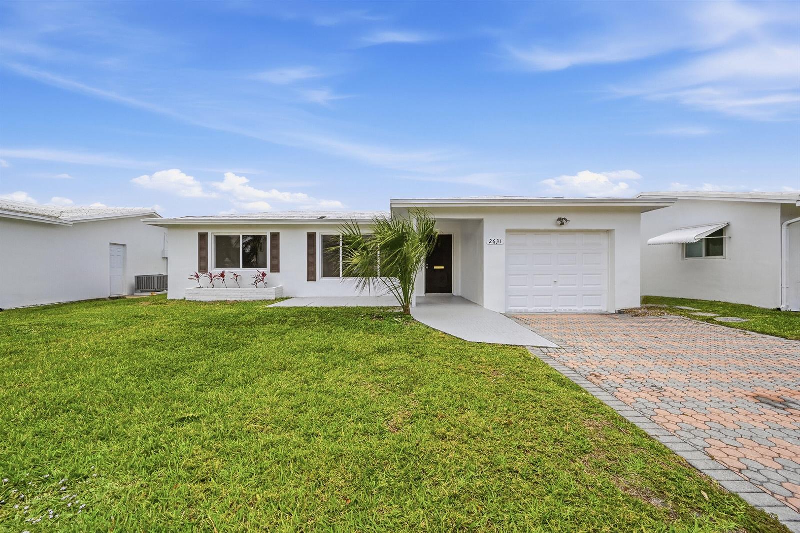 A white single-story house features a paved driveway, a small palm tree, and a lawn — 2631 W Golf Boulevard, Pompano Beach FL 33064, POMPANO BEACH, FL