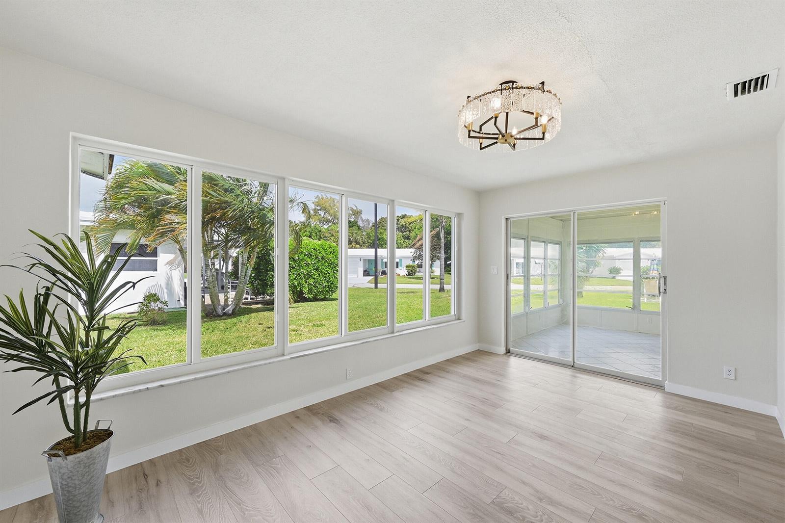 A bright, empty room features light wood-look flooring, large windows, and a glass sliding door — 2631 W Golf Boulevard, Pompano Beach FL 33064, POMPANO BEACH, FL