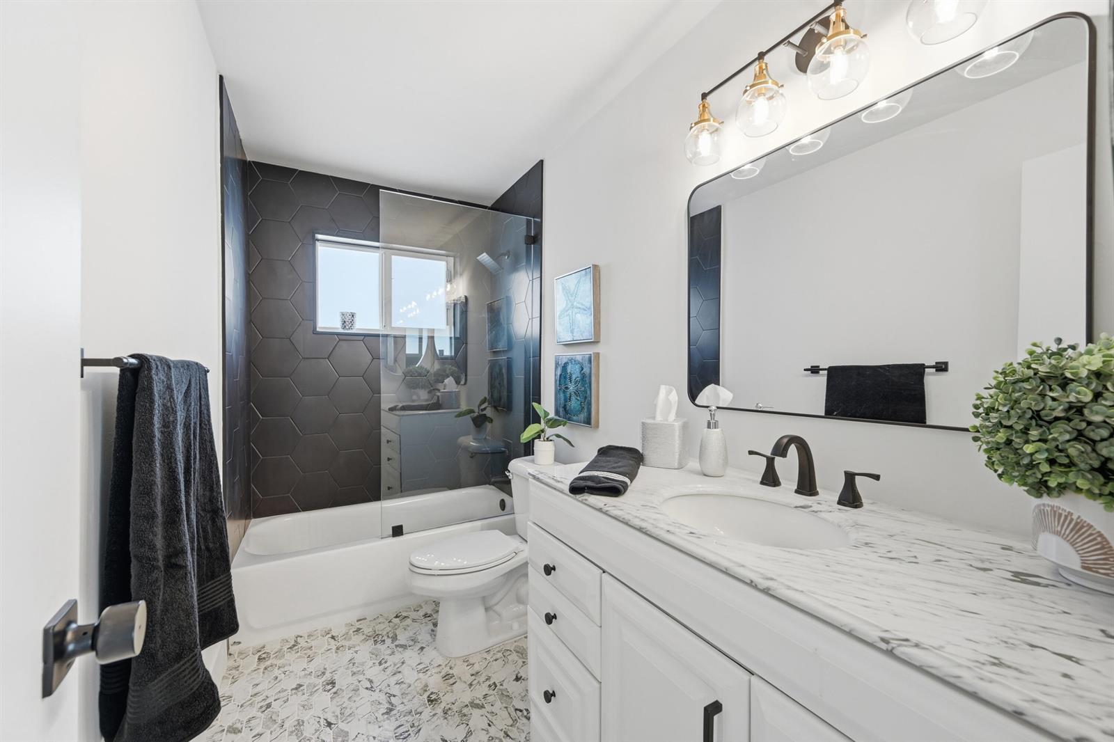 A modern bathroom features a white vanity, marble countertop, and a black hexagonal tile shower — 2631 W Golf Boulevard, Pompano Beach FL 33064, POMPANO BEACH, FL