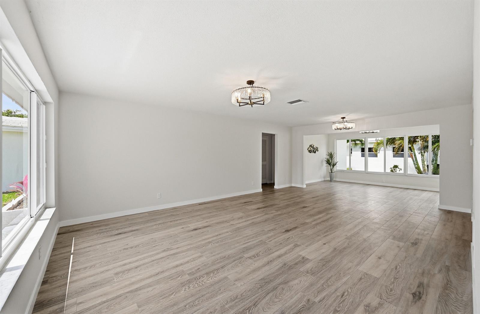 An empty living area features light wood-look flooring, white walls, and two crystal chandeliers — 2631 W Golf Boulevard, Pompano Beach FL 33064, POMPANO BEACH, FL